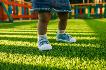 toddler in blue sneakers standing on bright green artificial grass in a colorful playground. low ang
