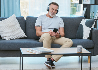 Fototapete - Man, headphones and smartphone on home sofa, comfortable and streaming online music or radio. Browsing, mobile and audio app in apartment with mature male person, weekend break and living room