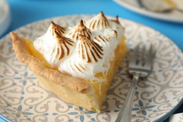 Wall Mural - piece of delicious pie with browned meringue and fork on light blue table, closeup