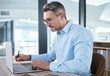 © peopleimages.com - Business, mature man and laptop with writing in notebook for company budget, accounting analysis and research. Financial analyst, employee and taking notes on taxes audit planning and strategy agenda