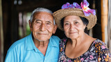 Pareja de adultos mayores latinos sonriendo juntos, ella con sombrero de flores, en un entorno rural

