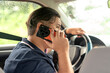 © Mdv Edwards - Middle-aged man in driver’s seat holds a phone to his ear while driving slowly, highlighting multitasking or distracted driving behavior.
