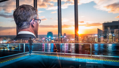 Poster - A double exposure of a man looking at the Hong Kong cityscape during sunset. The city lights and water reflect the vibrant sky.