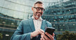 © CC/peopleimages.com - Business, smile and man in city, smartphone and internet with social media, message to contact and texting. Mature person, outdoor and low angle in street, cellphone or digital app for communication