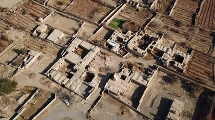 Drone video flying low above a traditional village with dense mudbrick houses, narrow walkways, and small courtyards, showing a preserved layout and close-packed community in a rural desert area.