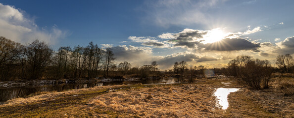 Wall Mural - a field with a river and a sun shining through the clouds