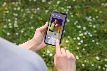Woman using mobile phone to listen to music outdoors, closeup. Open music player app on device screen