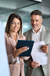 © insta_photos - Busy professional corporate business executives man and woman in suits holding tablet tech device having discussion working on digital project plan standing in office at team meeting. Vertical photo.