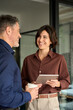 © insta_photos - Executive team of two business people working talking using tablet tech in corporate office. Happy professional business man and woman colleagues having conversation at work. Vertical photo.