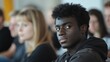 © Justlight - Young black man sitting attentively while listening to a political meeting or debate, surrounded by blurred figures in the background, reflecting on important social issues and civic engagement