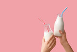 Hands clinking milk bottles with straws on pink background