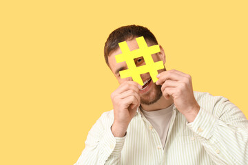 Funny young man with hashtag sign on yellow background