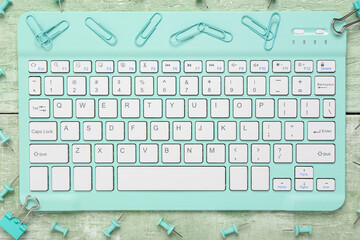 stylish cyan computer keyboard with clips on green wooden background