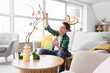 © Pixel-Shot - Happy boy in bunny ears decorating easter tree with colorful eggs in bright living room, he holds a glass jar with small decorative eggs while carefully placing an ornament on a branch