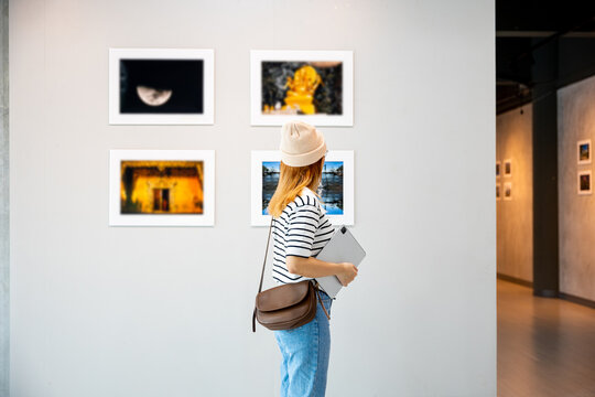Asian woman holding tablet at art gallery collection in front framed paintings pictures on white wall, Young person at photo frame hold digital book leaning against at show exhibition artwork gallery