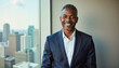 © f_bossa - Modern portrait headshot of a friendly ceo executive business worker: A smiling, middle-aged Black man in a suit confidently poses indoors with a city skyline visible through a large window behind h