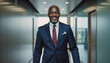 © f_bossa - Modern portrait headshot of a friendly ceo executive business worker: A confident, distinguished Black man in a navy suit and red tie stands smiling in a modern office hallway.