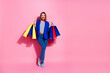 © deagreez - Smiling young woman holding colorful shopping bags against pink background while dressed in stylish casual attire