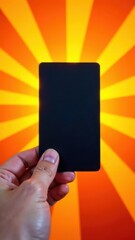 Poster - A person extends a blank black card towards the viewer set against a striking orange background with radiant rays. The scene evokes curiosity and creativity inviting imagination.