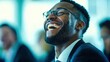 © NovaVision - An african american businessman laughs heartily, sharing joy and positivity in a work environment.