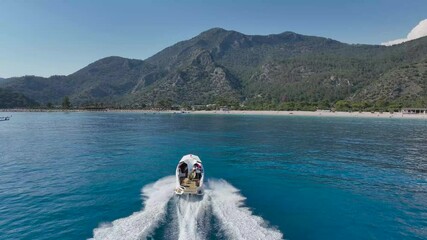 Wall Mural - Aerial footage of a speedboat going towards green mountain on a sunny day with blue sky