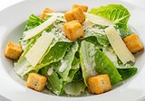A refreshing Caesar salad, a vibrant mix of crisp romaine lettuce, crunchy croutons, and creamy dressing, garnished with delicate parmesan shavings, presented on a pristine white plate.