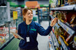 © Drazen - Happy female worker checking stock on product shelves at supermarket.