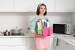 © Pixel-Shot - Young woman holding basket with cleaning supplies in kitchen