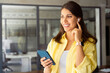 © Stock 4 You - Smiling young indian specialist, female manager using cell phone mobile earphones for work conversation call. Happy latin hispanic business woman working online on smartphone standing in modern office
