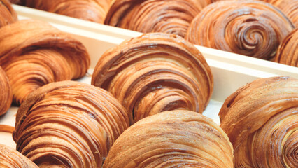 Poster - A row of croissants are displayed in a bakery. croissants are golden brown and have a flaky, buttery texture. display is arranged in a way that highlights the variety of shapes