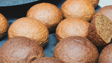 Poster - A row of brown and white bread rolls on a black plate. The brown rolls are slightly larger than the white ones