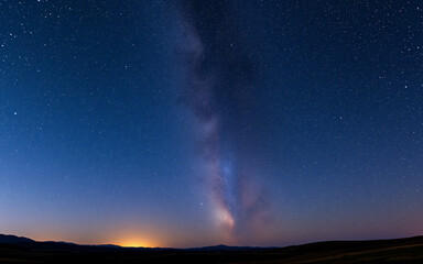 Wall Mural - night sky displays the milky way arcing above a dark horizon. stars illuminate the vast expanse abov