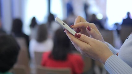 Woman is looking at her cell phone in a crowded room. The people around her are watching her