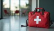© miss irine - Red first aid kit with white cross sign rests on floor. Medical emergency, healthcare, safety, rescue concepts. Portable equipment supplies basic medical treatment, injury care in home or workplace.