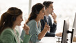 © fizkes - Serious Latin telephone assistant woman sitting at workplace with contact center colleagues, talking to client on audio call, using headset and computer, giving assistance, support. Banner shot