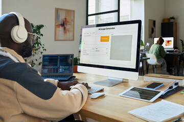 Fototapete - Young African American software developer testing AI image generation program on desktop computer and laptop