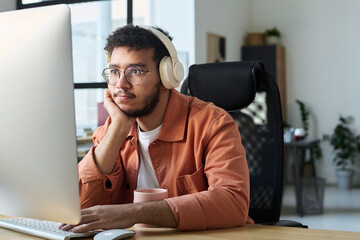 Poster - Young serious man in headphones looking at computer screen and keeping hand on keypad while watching online video