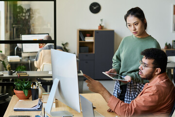 Fototapete - Young male programmer pointing at computer screen while discussing ways of decoding data with female colleague at meeting