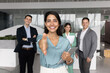 © fizkes - Happy Latin business leader woman offering handshake at camera, posing for portrait with group of colleagues in background, welcoming for hiring, career start, joining successful team