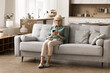 © fizkes - Home comfort and staying in touch. Old age woman housewife in retirement rest on cozy couch at quiet peaceful house texting messages on mobile phone browse web for news make purchases at online store