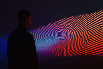 Poster - Man Contemplating Abstract Display: An anonymous individual gazes intently at a dynamic display of undulating lines and vibrant colors, creating an immersive experience of light and form.