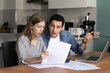 © fizkes - Married couple sit at table in kitchen, analyzing financial documents with surprised or concerned expressions. Family calculating expenses, reviewing bills, dealing with unexpected financial issues