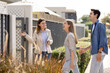 © fizkes - Friendly realtor agent welcoming young excited Hispanic married couple at entrance of modern residential property, showcasing new home for sale or rent. Real estate consultation, homeownership, dream