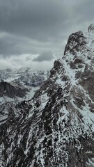 Wall Mural - aerial view of amazing rocky mountains in snow under moody gray clouds, dolomites, italy. vertical v