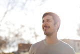 Portrait of young man gazes forward with soft smile, sunlit from behind. Conveys hope, purpose, clarity, great for wellness, mindset, coaching or future vision concepts. Horizontal, glowing background