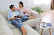 © New Africa - Couple with gadgets resting on sofa in living room
