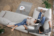 © New Africa - Couple with tablet resting on sofa in living room, above view