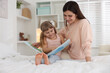 © New Africa - Bedtime. Happy little daughter reading book with her mother on bed at home