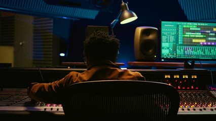 Poster - African american sound producer connecting coiled cable on mixing console, processing and editing old recordings. Technician pressing switchers and sliders to create music. Camera B.