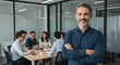 © Matheus - A confident man stands smiling with arms crossed in a modern office, while a diverse team engages in a collaborative meeting in the background.